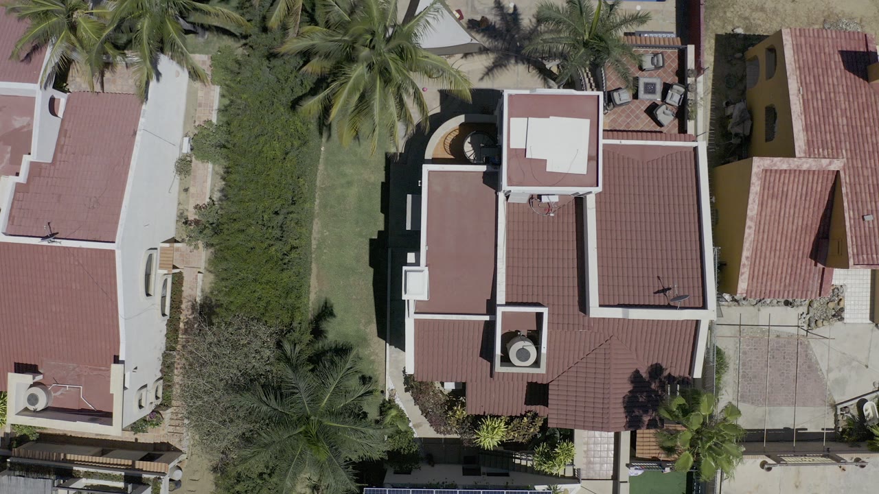 Overhead view of red tile roofs, trees, lawn, and driveway paving.