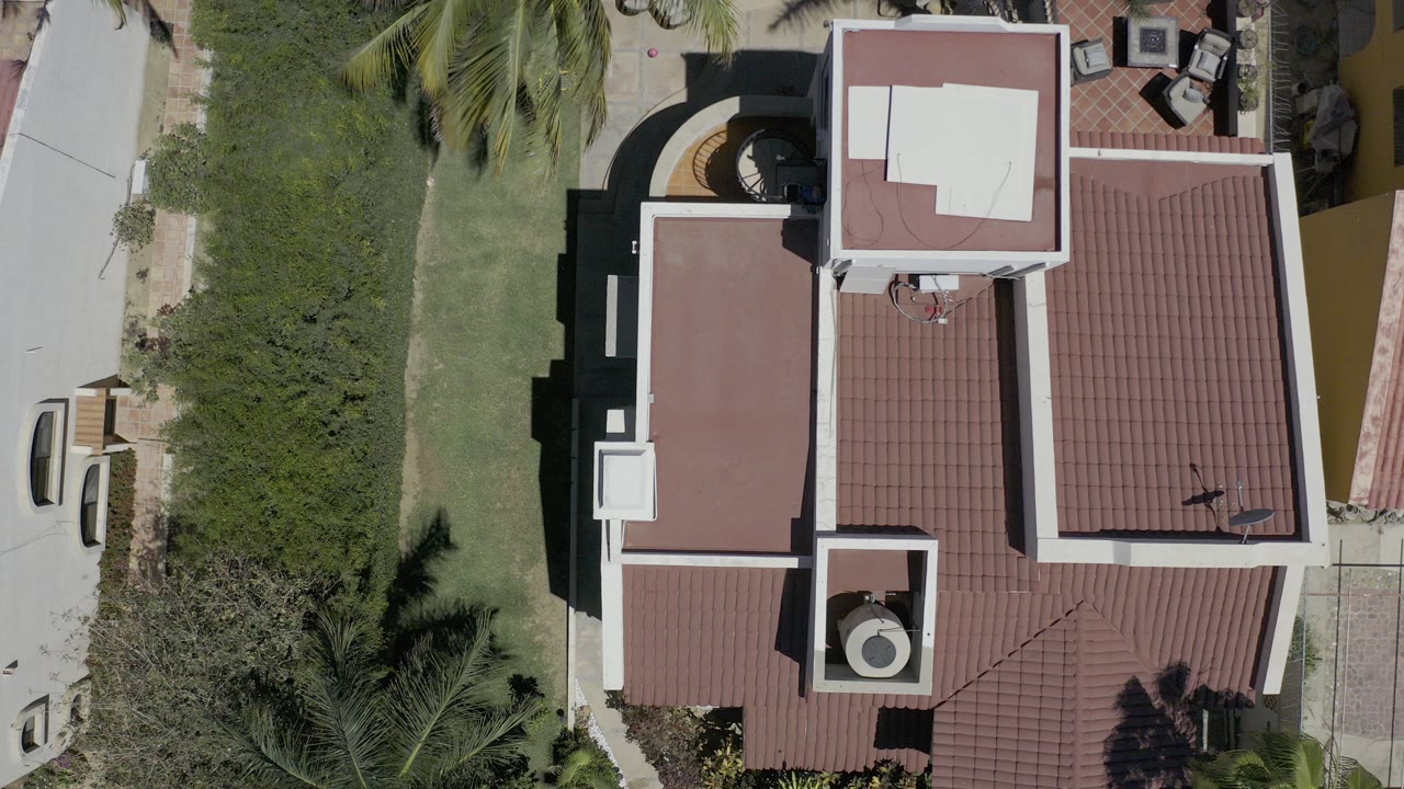 Overhead view of a white building with a red roof beside lawn and palms.