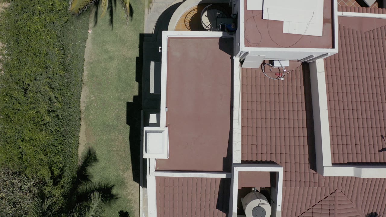 Overhead view of a red-roofed house beside lawn and hedges.
