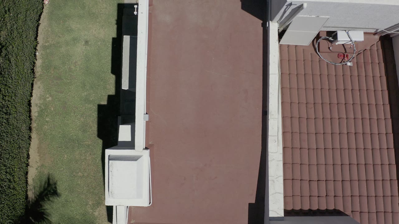 Closer top-down view of red roof, white walls, lawn, and tiled roof edge.