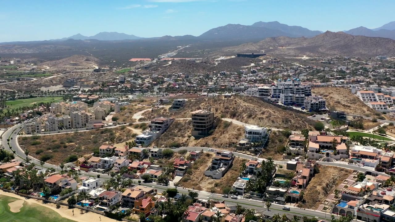 Wide aerial of homes and unfinished hillside lots under clear sky.