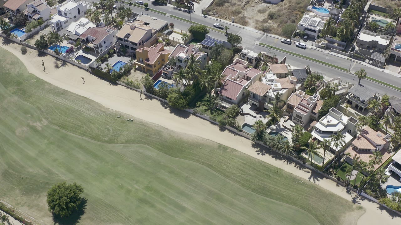 Aerial view of golf course fairway, villas, pools, palm trees, and a road.