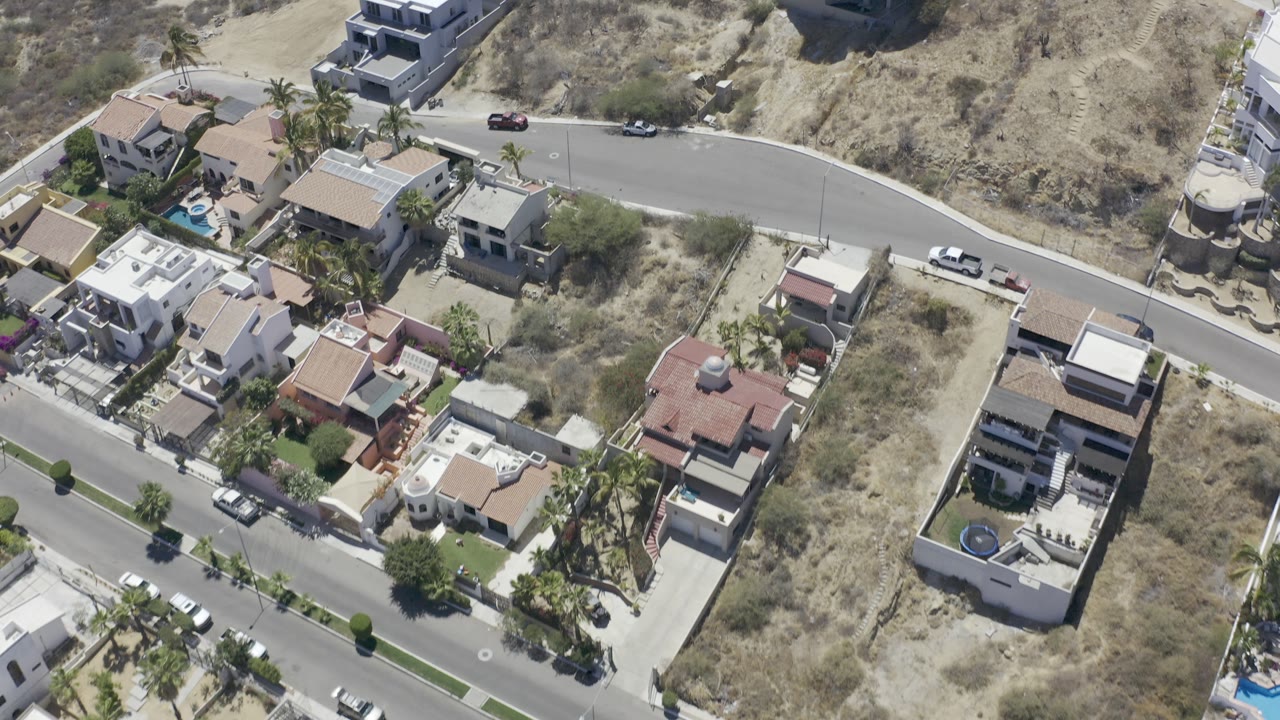 Drone view of hillside homes along a curved road in bright sun.