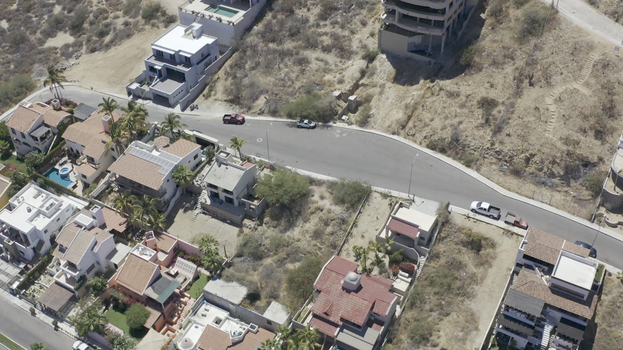 Aerial view of houses beside a curved road and dry hillside.
