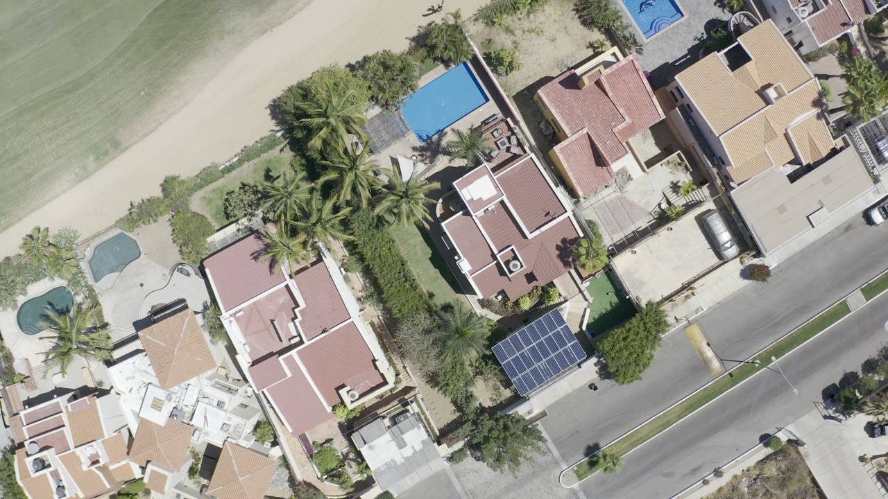 Overhead view of homes, palm trees, pools, and a road.