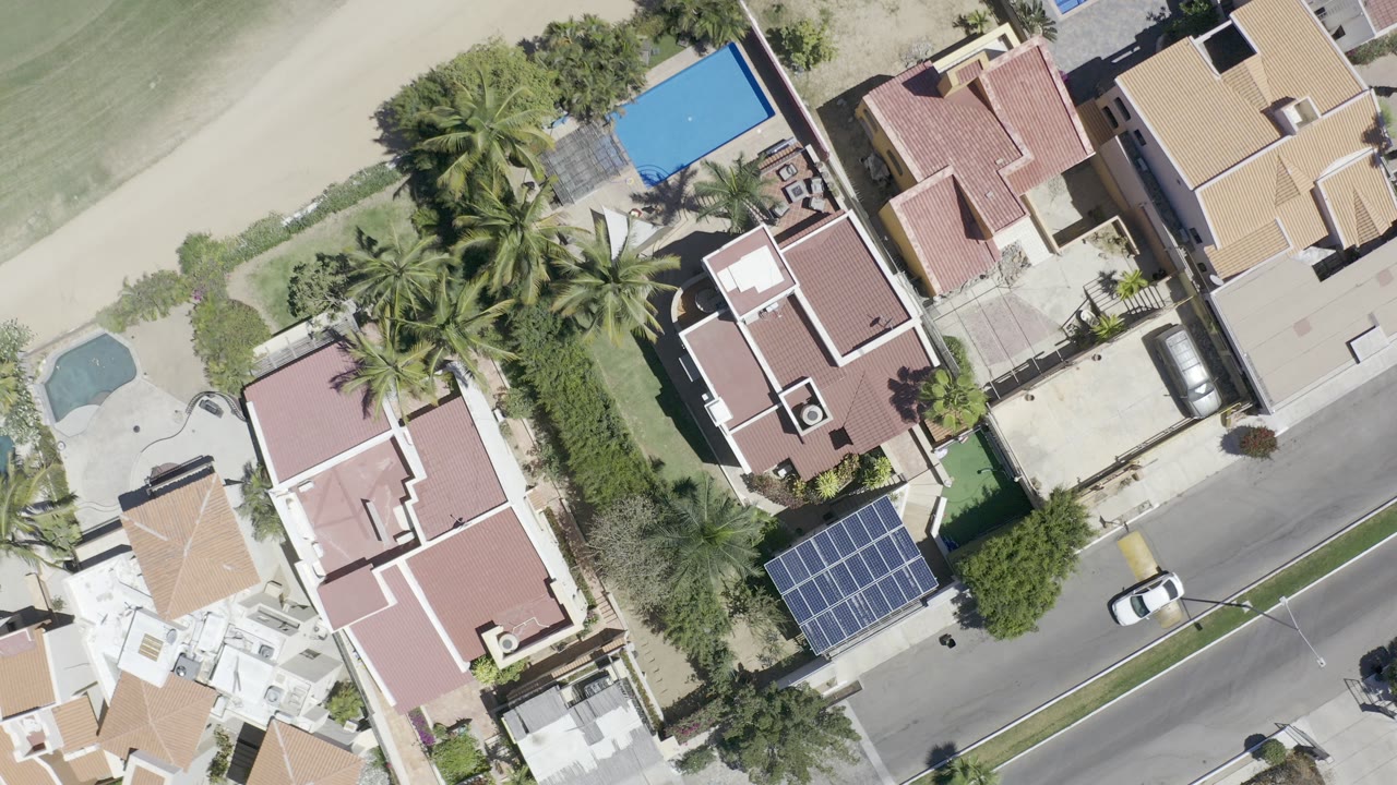 Top-down aerial view of beachfront homes, pool, palms, road, and solar panels.