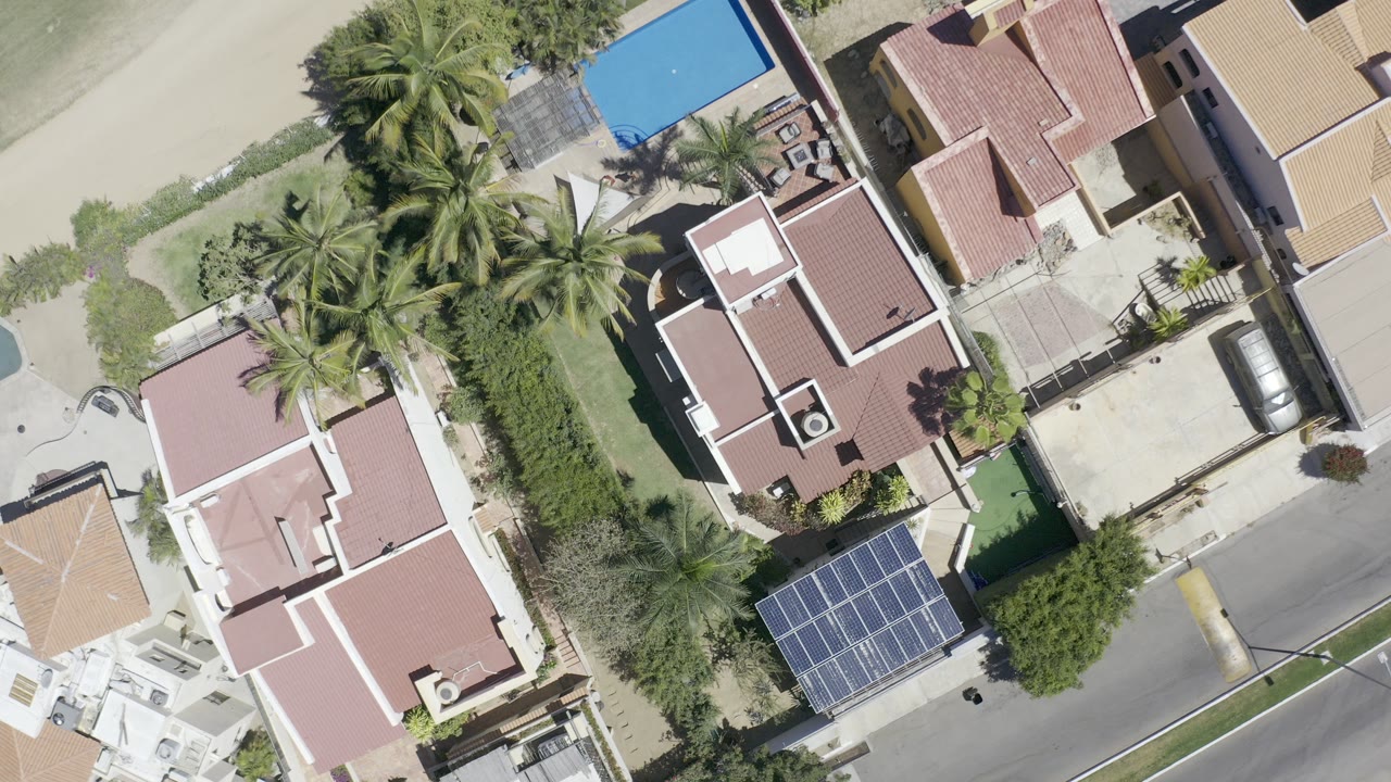 Overhead view of tile-roof houses, palms, a street, and a blue pool.