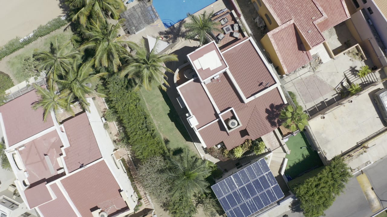 Top-down aerial of red-roofed homes, palms, pool water, and solar panels.