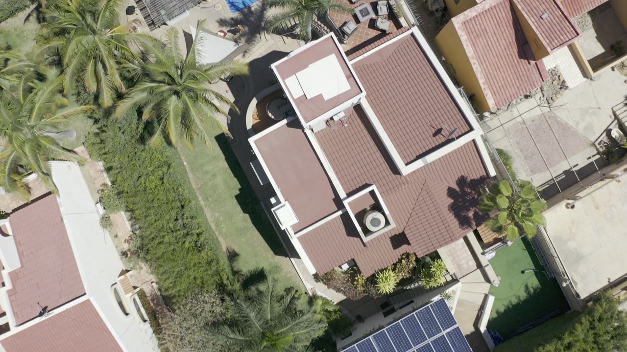 Overhead view of red tile roofs, palms, hedges, and driveways.