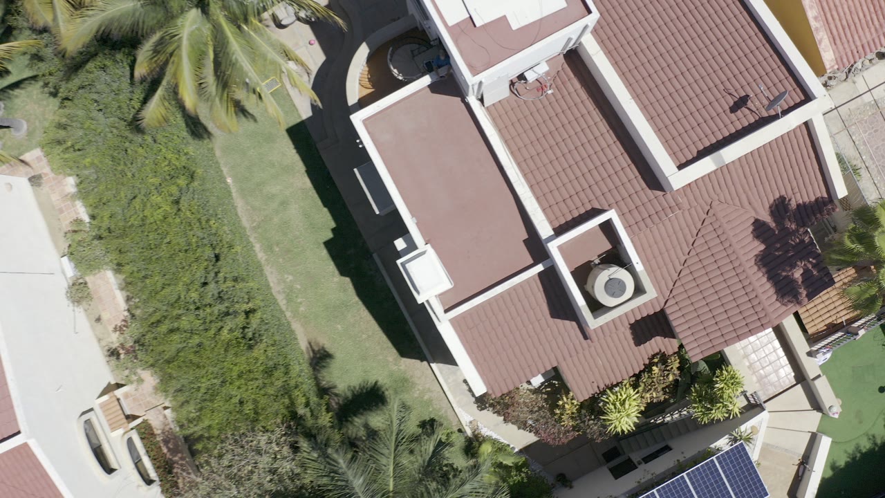 Overhead view of red tile roofs, lawn, shrubs, and palm fronds.