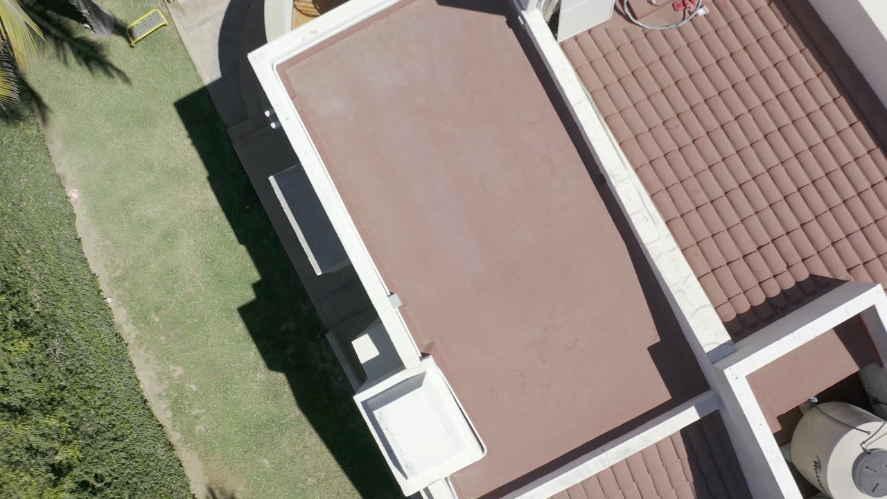 Overhead view of brown flat roof beside grass and tiled roof