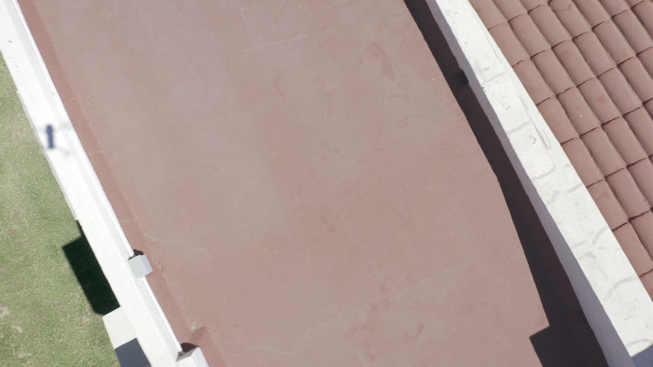 Top-down view of a red roof beside a white parapet and terracotta tiles.