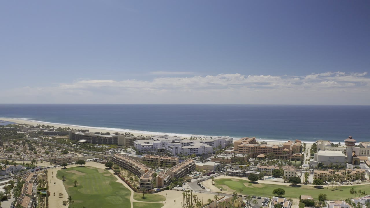 Aerial view of resort buildings, golf greens, beach, and ocean horizon.