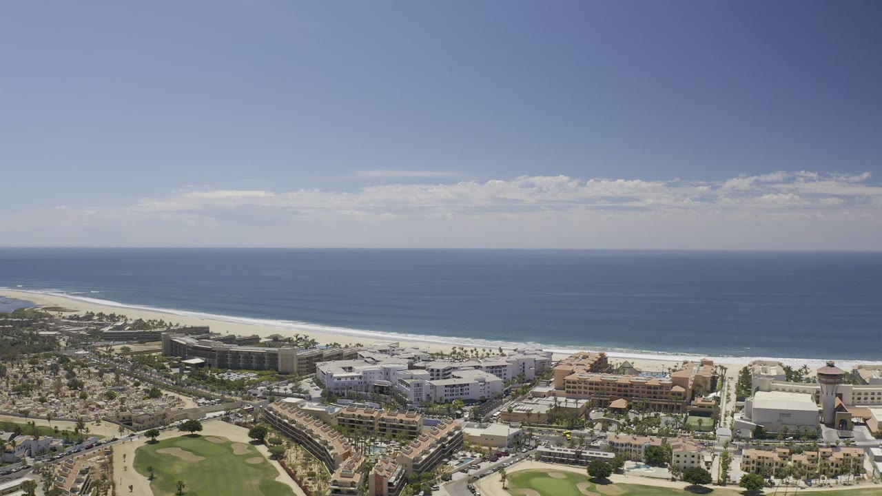 Wide aerial of Los Cabos shoreline with buildings, roads, beach, and ocean.