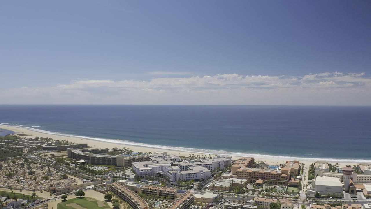 Coastal aerial looking over buildings, beach, and open ocean.