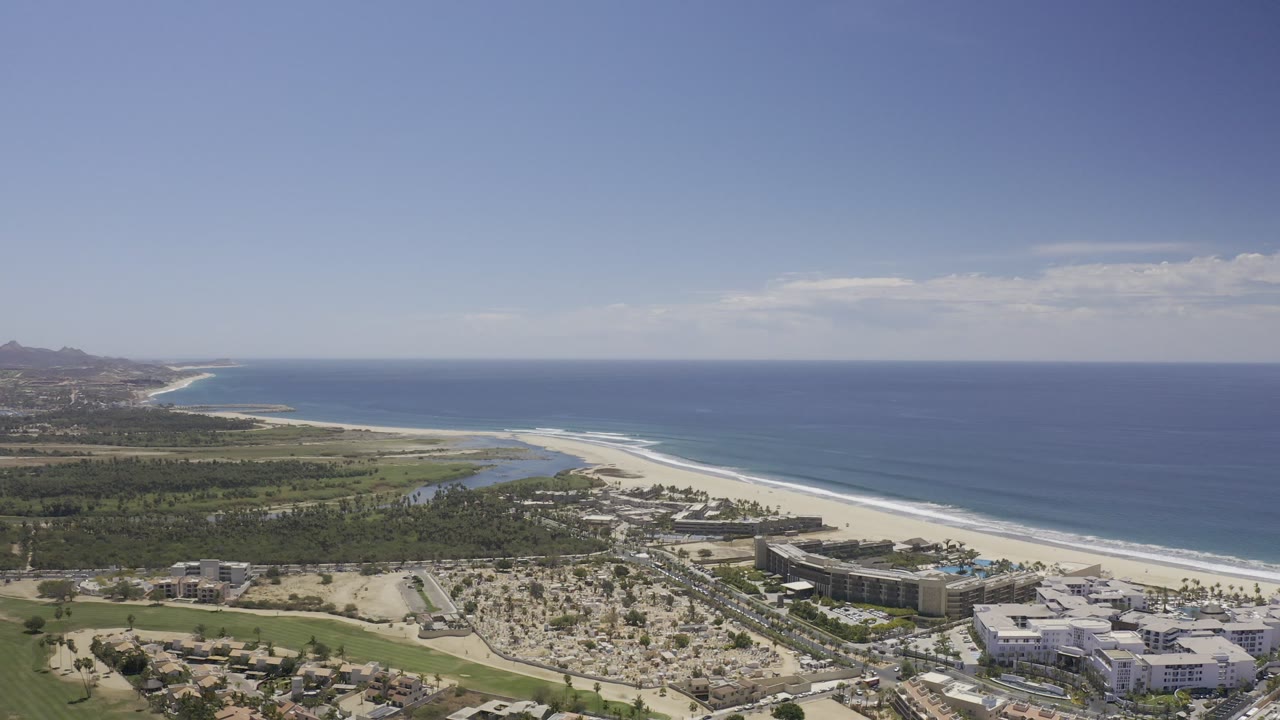 Aerial view of coastline, beach, resort buildings, and blue ocean.