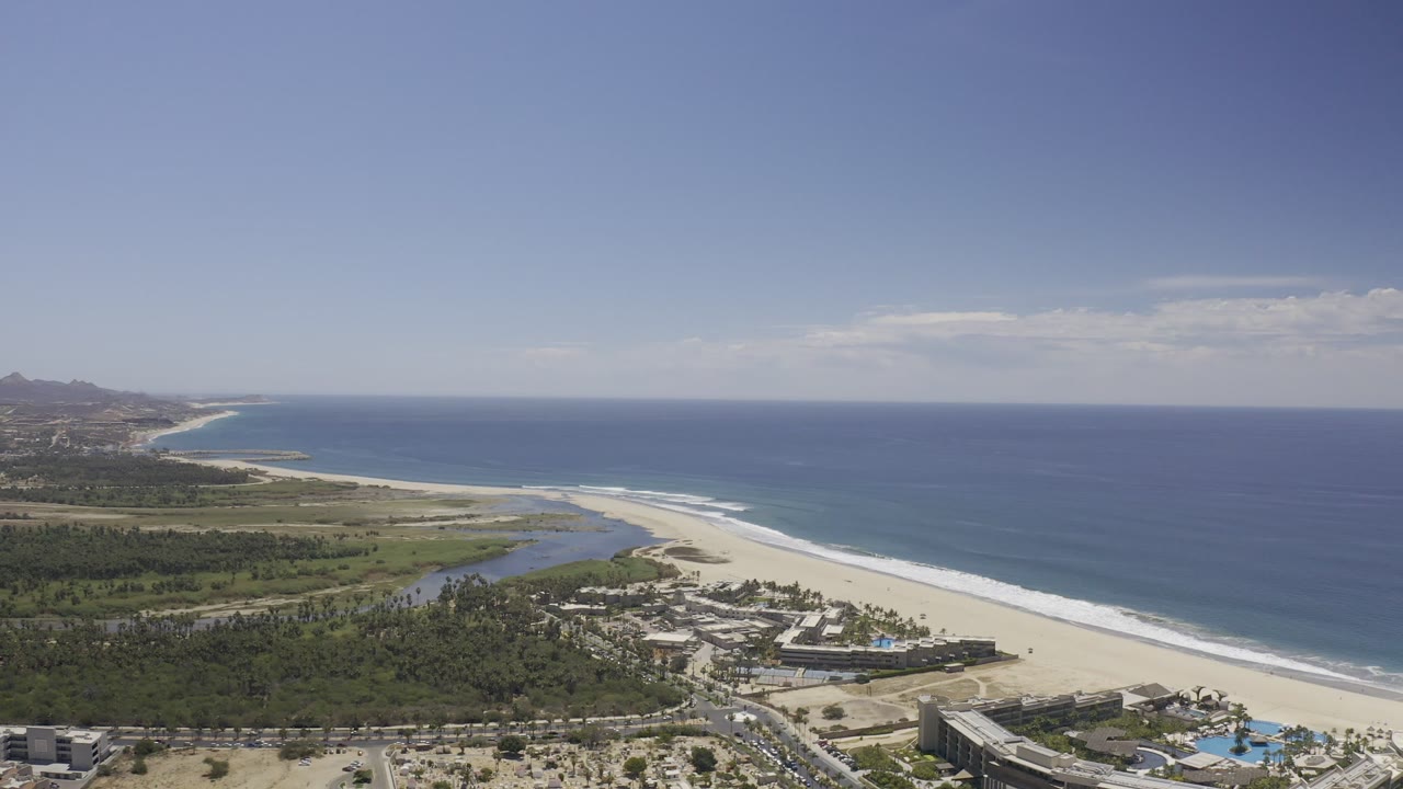Aerial view of beach, ocean, lagoon, palms, and resort buildings.