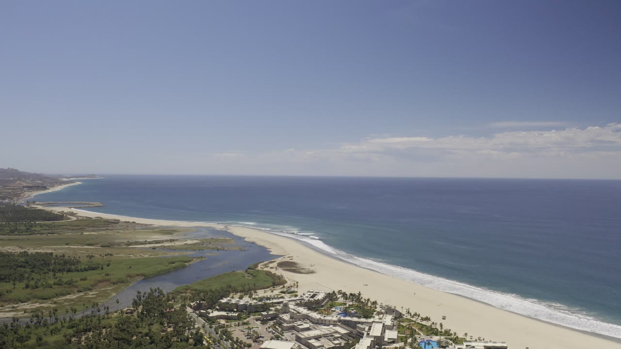 Drone-style coastal view with beach, ocean, and inland waterway.