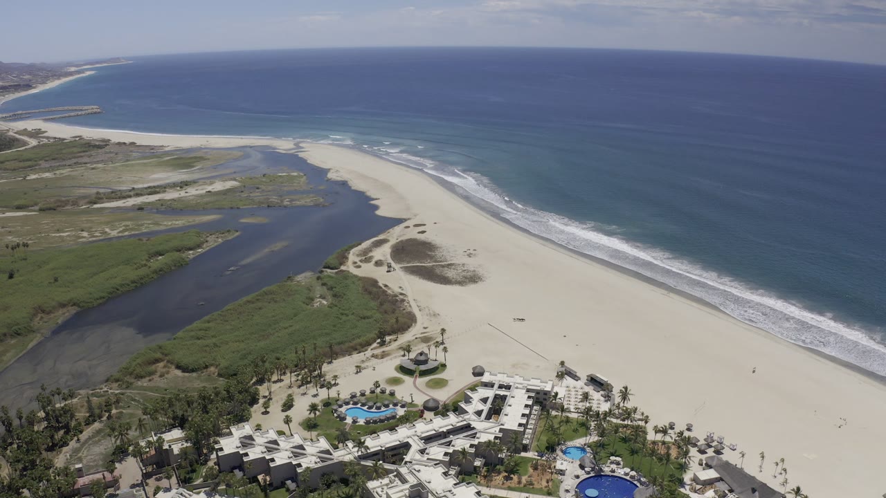 Wide drone view of beach, inlet, resort, and ocean.