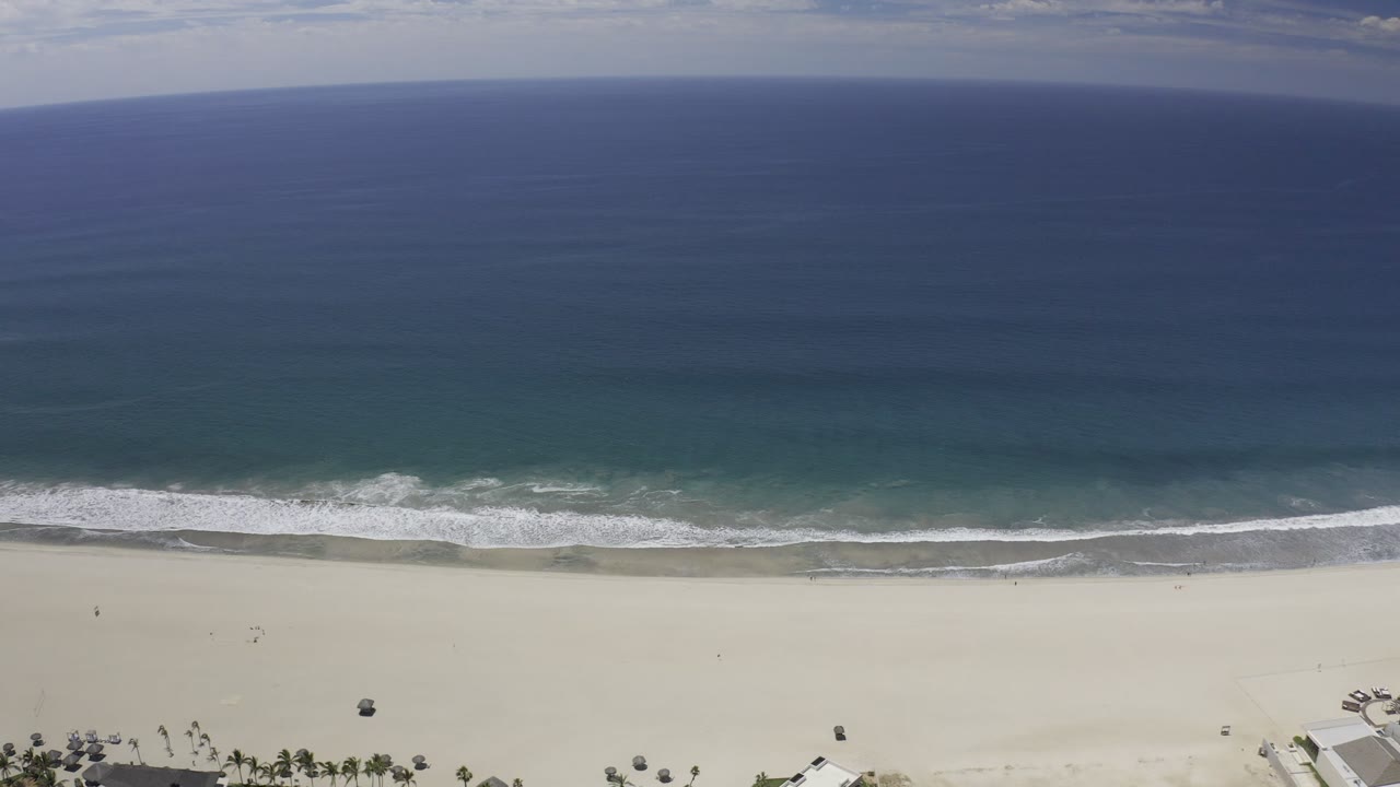 Blue ocean and white waves meeting a broad sandy beach.