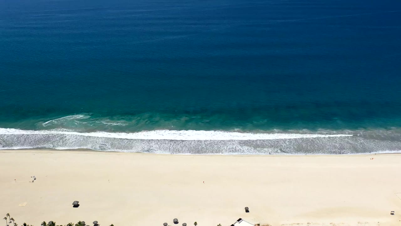 Top-down view of surf rolling onto pale beach