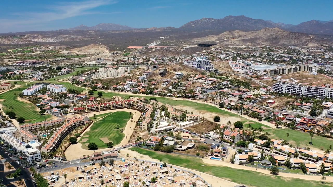 High drone view across houses, roads, golf greens, and mountain ridges