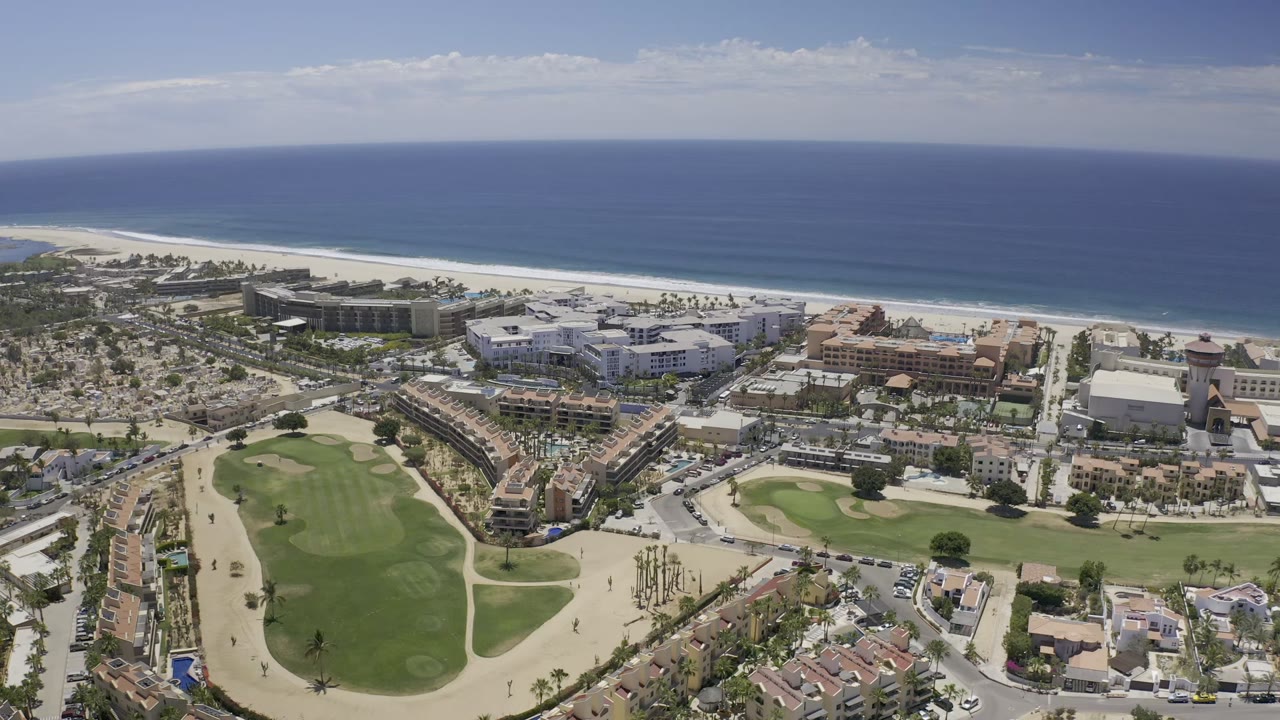 Aerial view of golf-course greenery, beachfront buildings, beach, and ocean