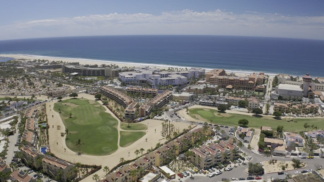 Coastal aerial over resort area, golf greens, roads, beach, and sea