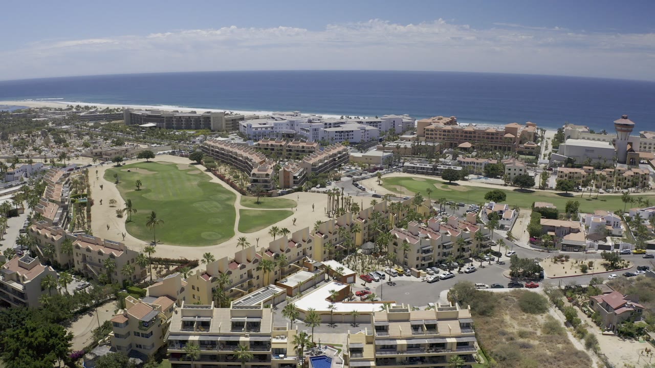Aerial view of coastal buildings, green lawns, roads, and ocean horizon.