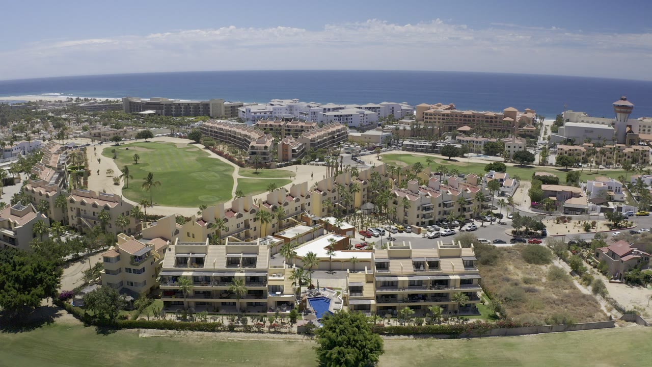 Aerial view over golf course grass, apartment buildings, hotels, and ocean horizon.