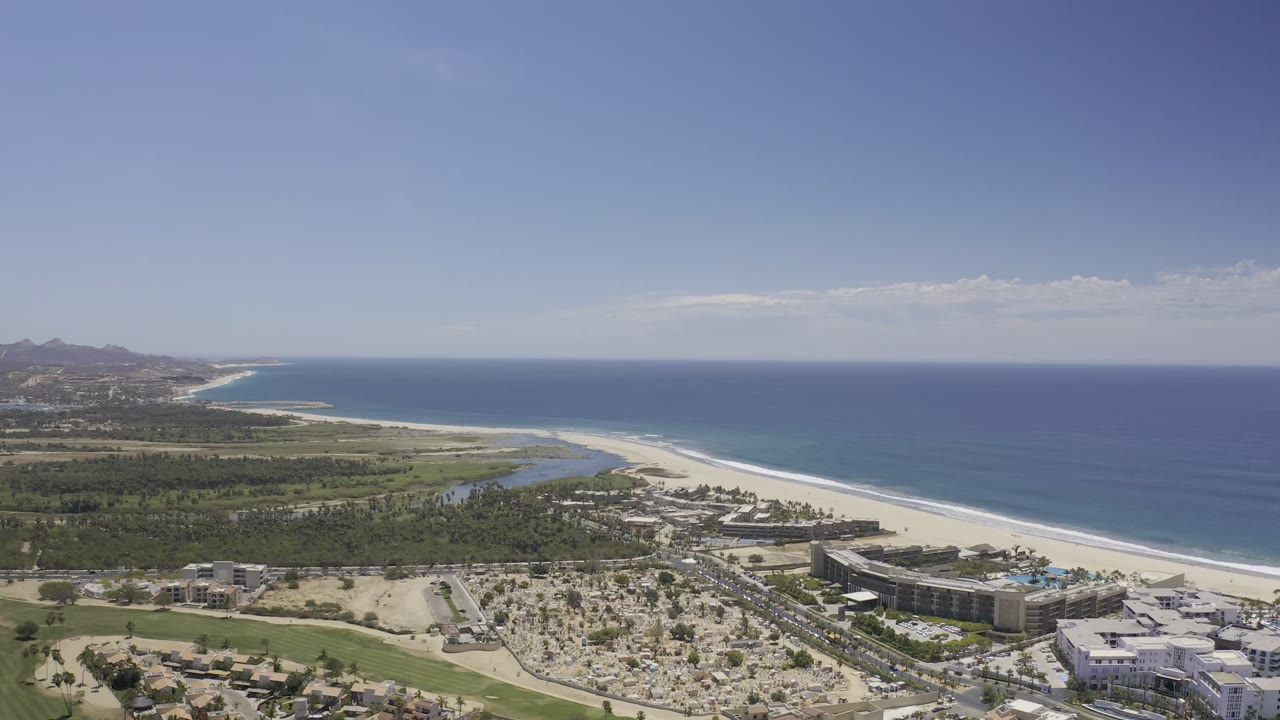 Aerial view of beach, ocean, coastal buildings, and inland greenery.