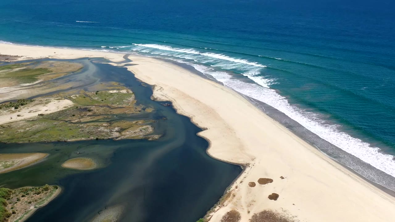 High aerial view of empty sand, green wetlands, and ocean surf.