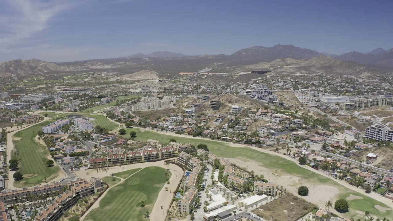 Aerial view of city buildings beside green fields and dry hills.