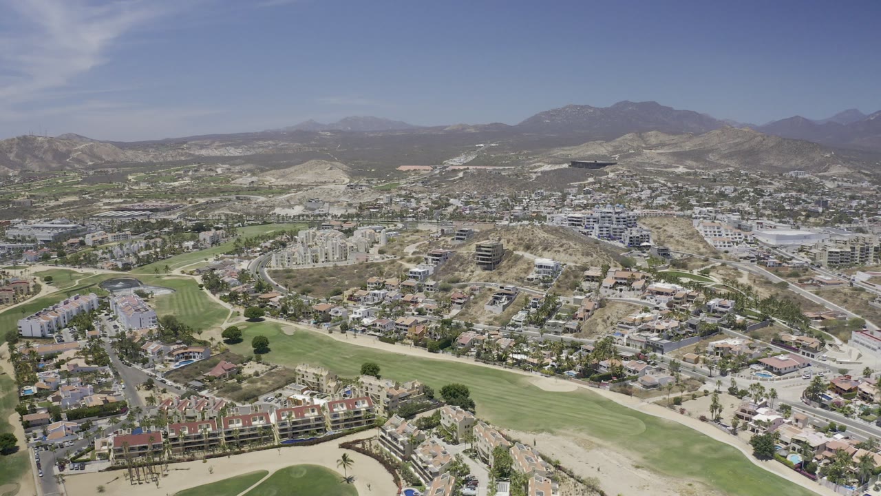 Aerial view of golf fairways, roads, buildings, desert hills, and distant mountains.