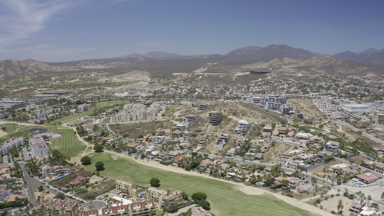 Broad aerial panorama of city buildings, golf course, and mountains.