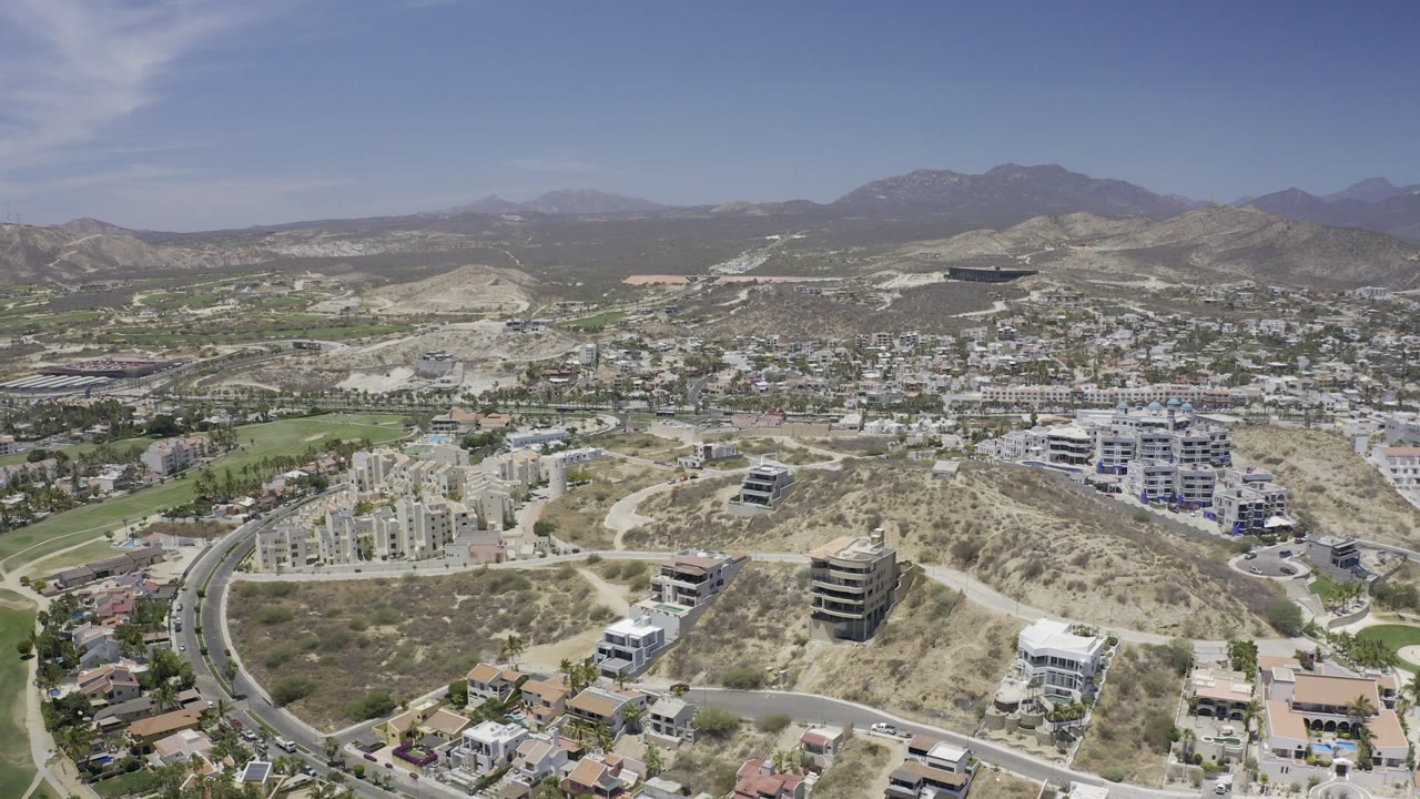 Aerial view of dry hills, roads, buildings, green space, and distant mountains.