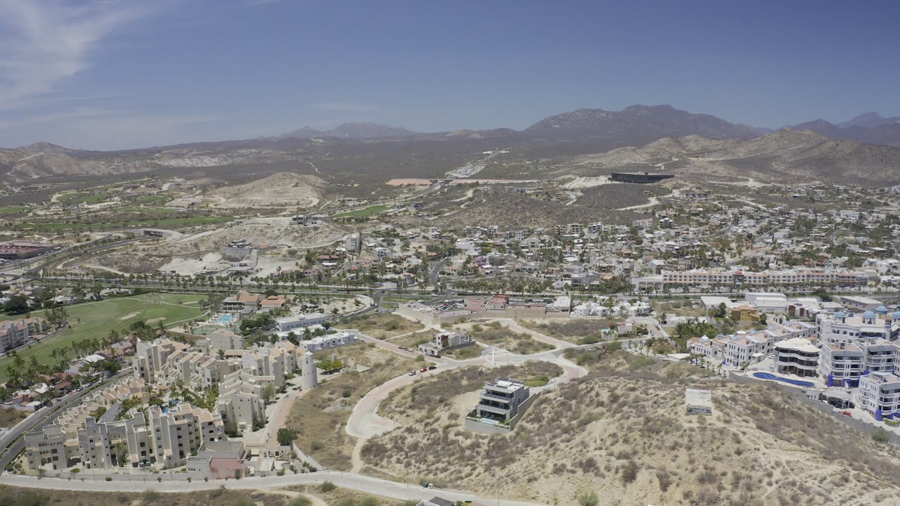 Aerial view of hillside city blocks, roads, golf green, and mountains.