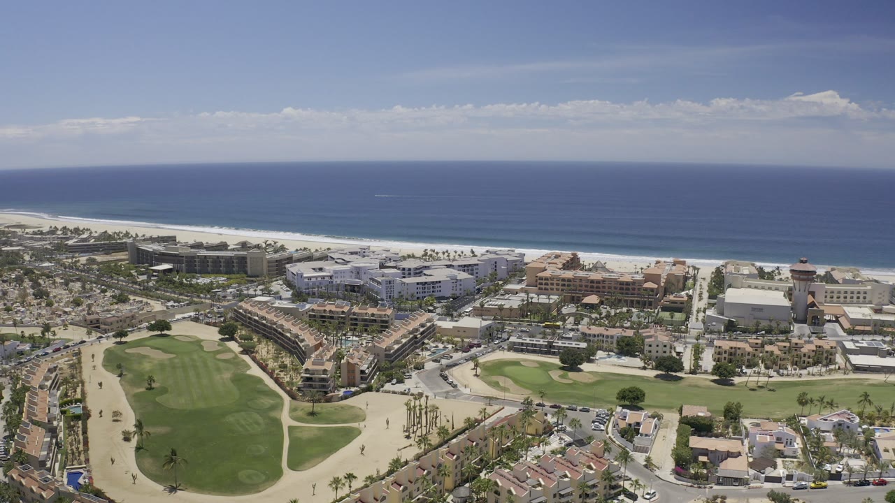Aerial view of golf greens, coastal buildings, beach, and ocean.