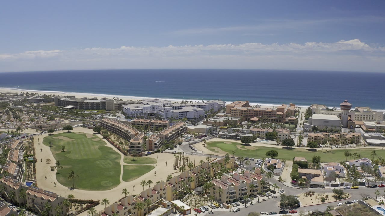 Aerial view of coastal buildings, lawns, streets, and ocean horizon.