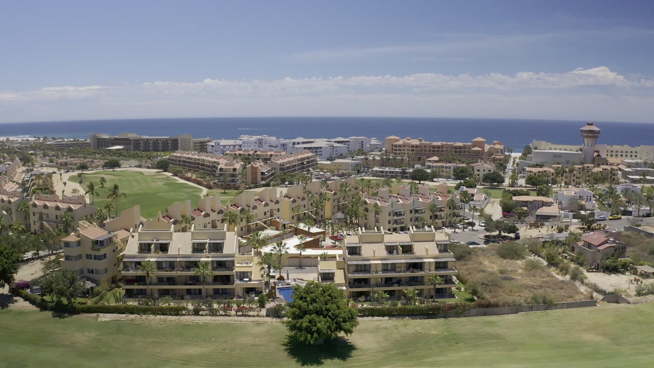 Aerial view of green fairway, coastal buildings, and ocean horizon.