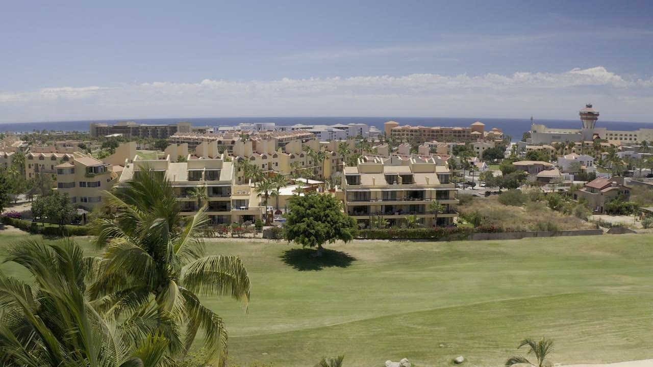 Wide resort-area view with palm leaves, fairway, buildings, and ocean