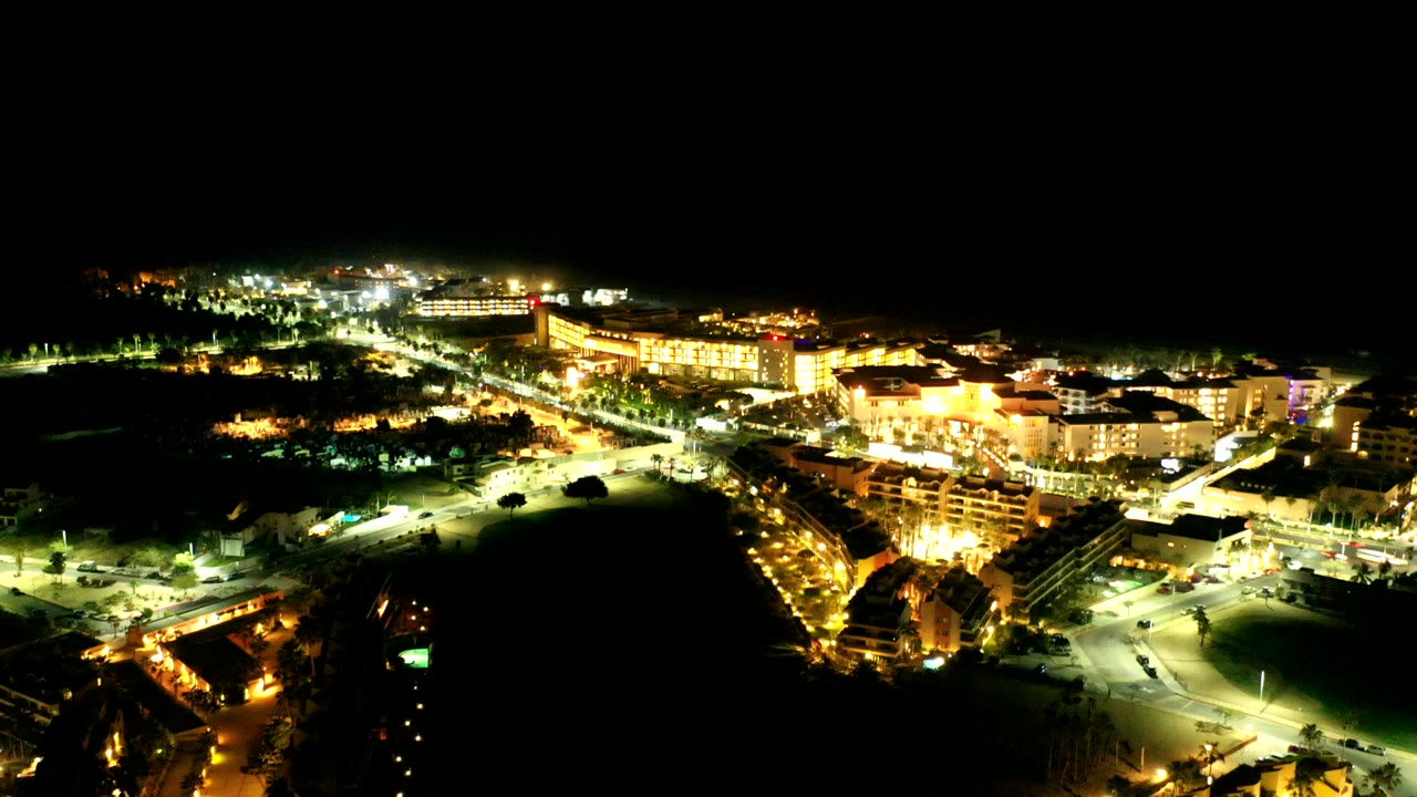 Night aerial view of illuminated city roads and buildings under a black sky.