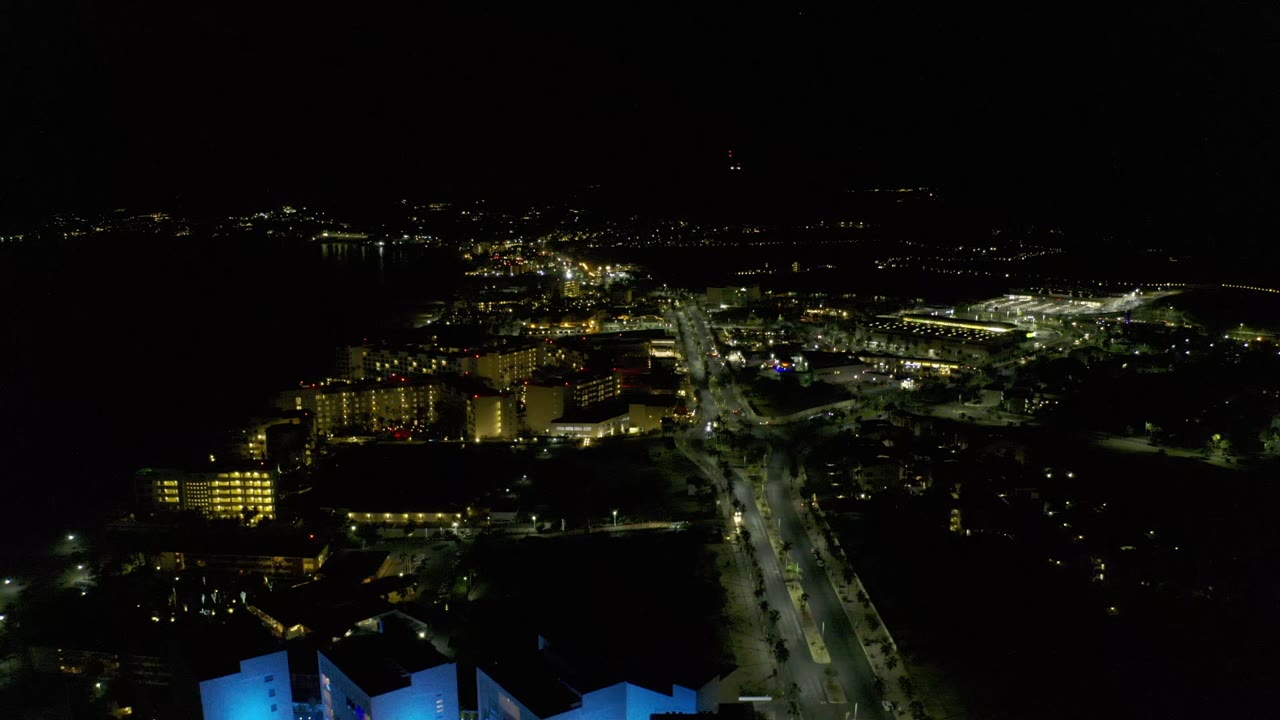 Dark aerial cityscape with a lit road and hotel-like buildings.
