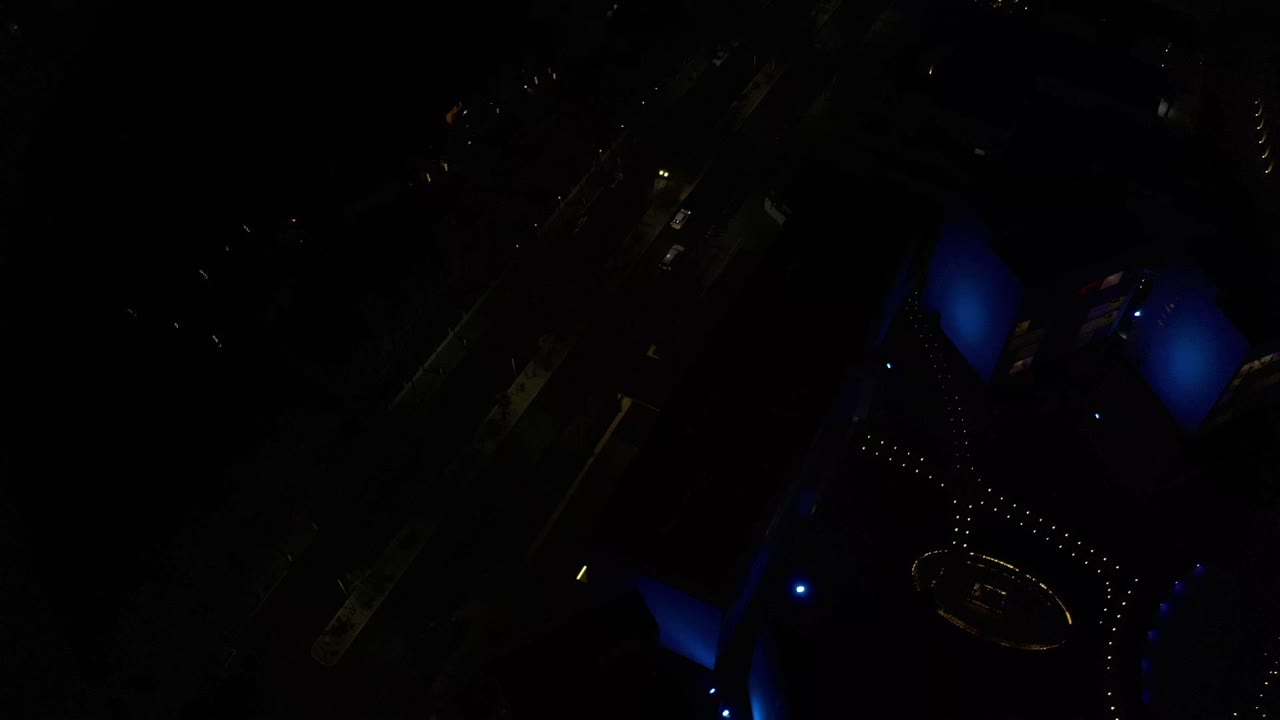 Overhead nighttime view in Los Cabos, Mexico, with blue-lit building forms, dotted exterior lights, deep shadows, and no visible people.