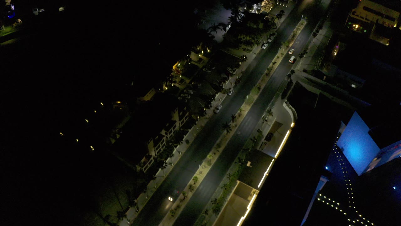 Night aerial view of a lit road beside dark water and buildings.