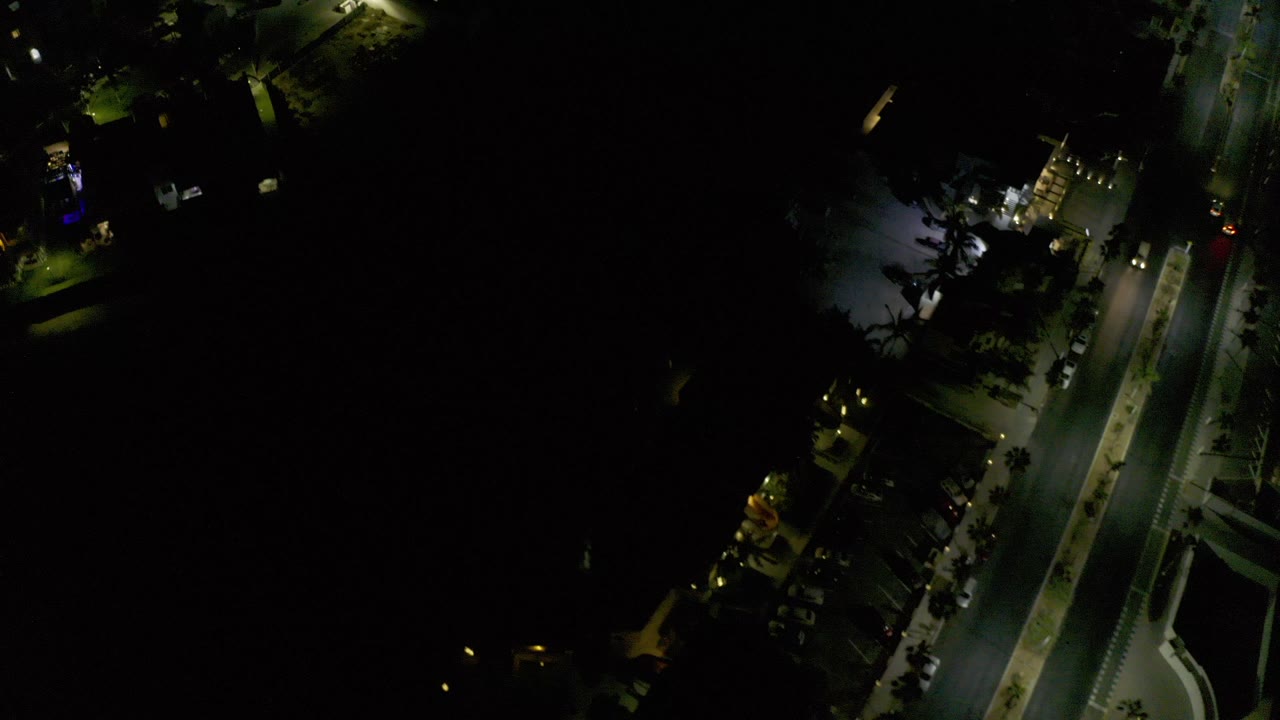 Top-down night view of a lit road and dark neighborhood blocks.
