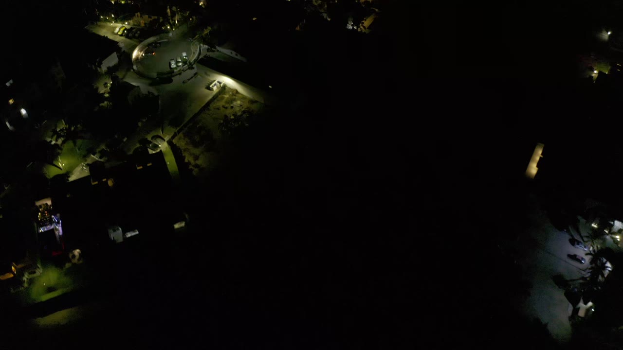 A later aerial frame over Los Cabos, Mexico, keeps the circular lit area near the top while scattered streetlights and tree shadows fill the darker lower frame, with no visible people.