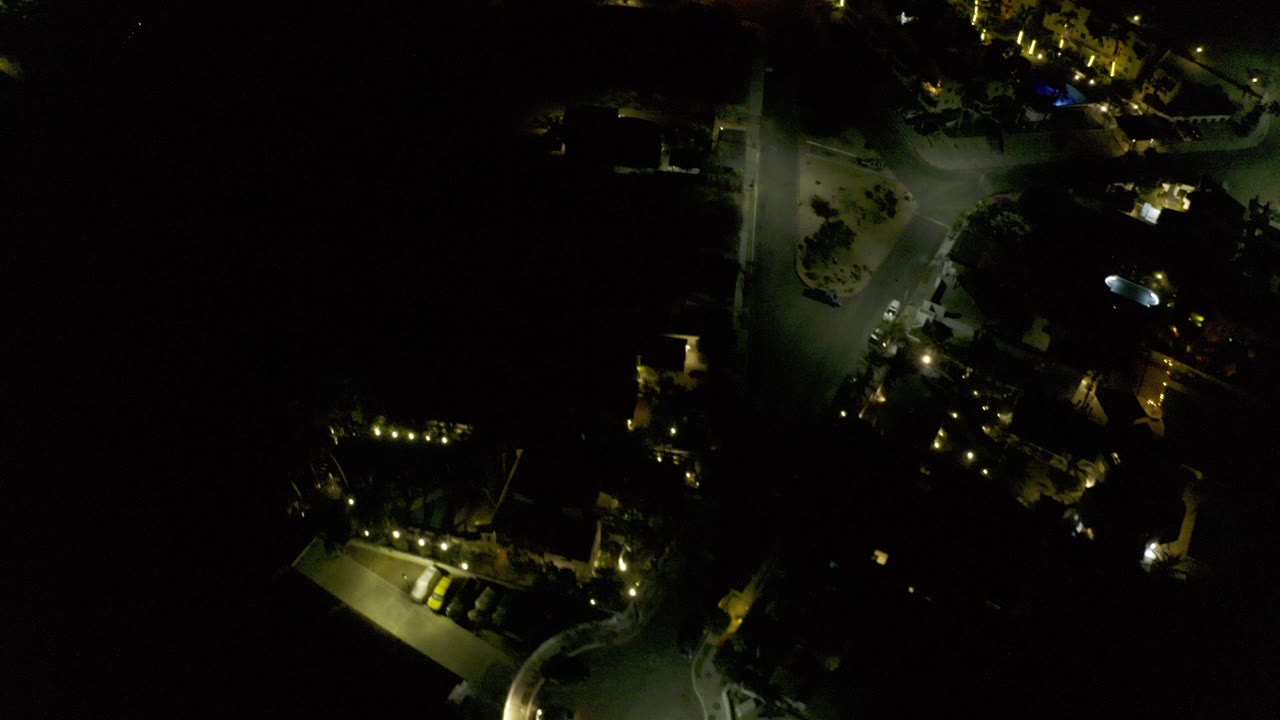 Night aerial view of lit streets and homes surrounded by darkness.