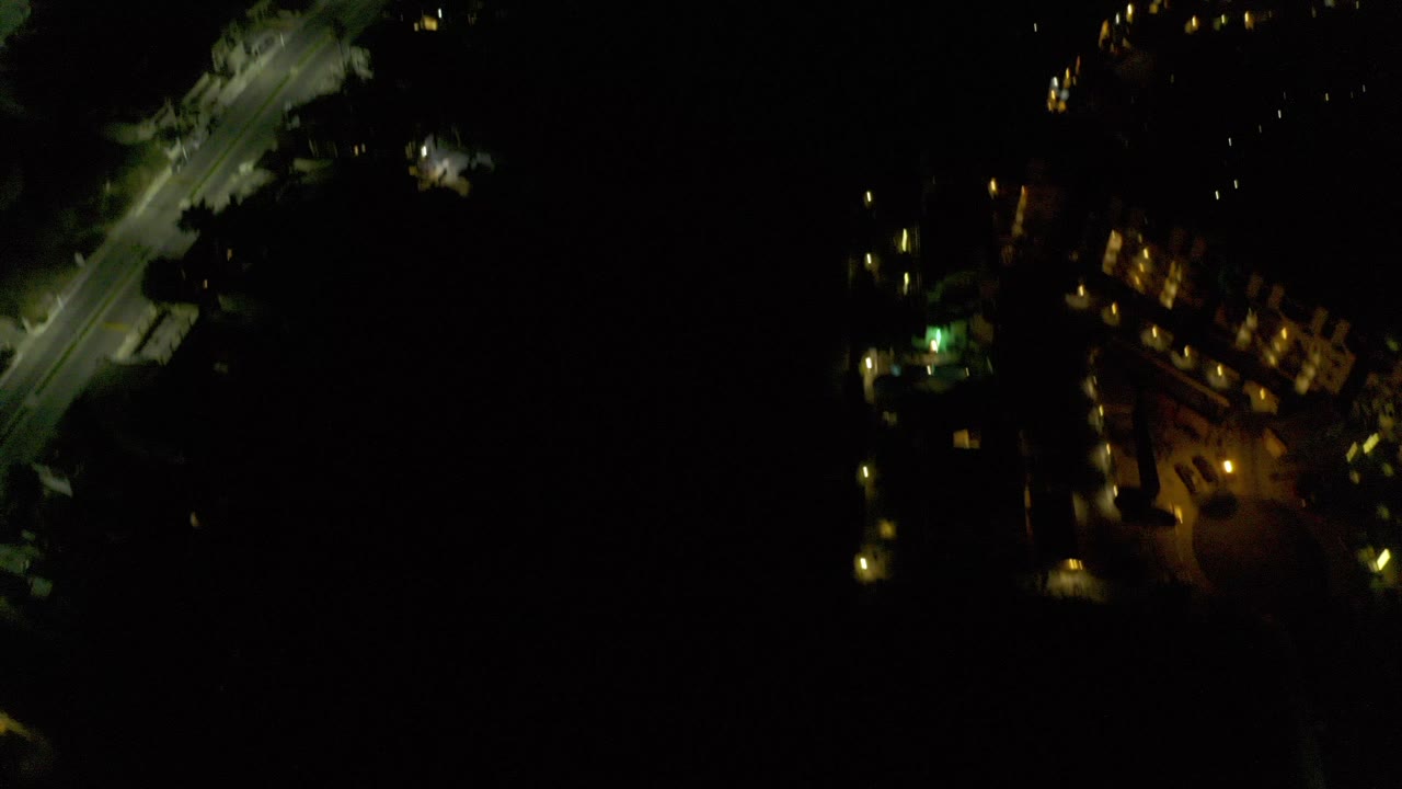 Opening aerial night frame over Los Cabos, Mexico, with a diagonal lit roadway, scattered building lights, large black areas, and no visible people.