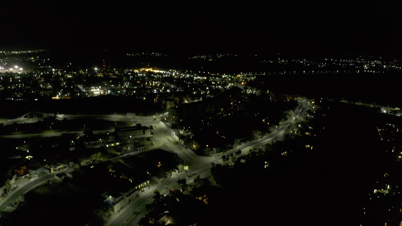 Opening frame of Los Cabos at night from above, showing lit roads and scattered city lights below a large black sky with no visible people.